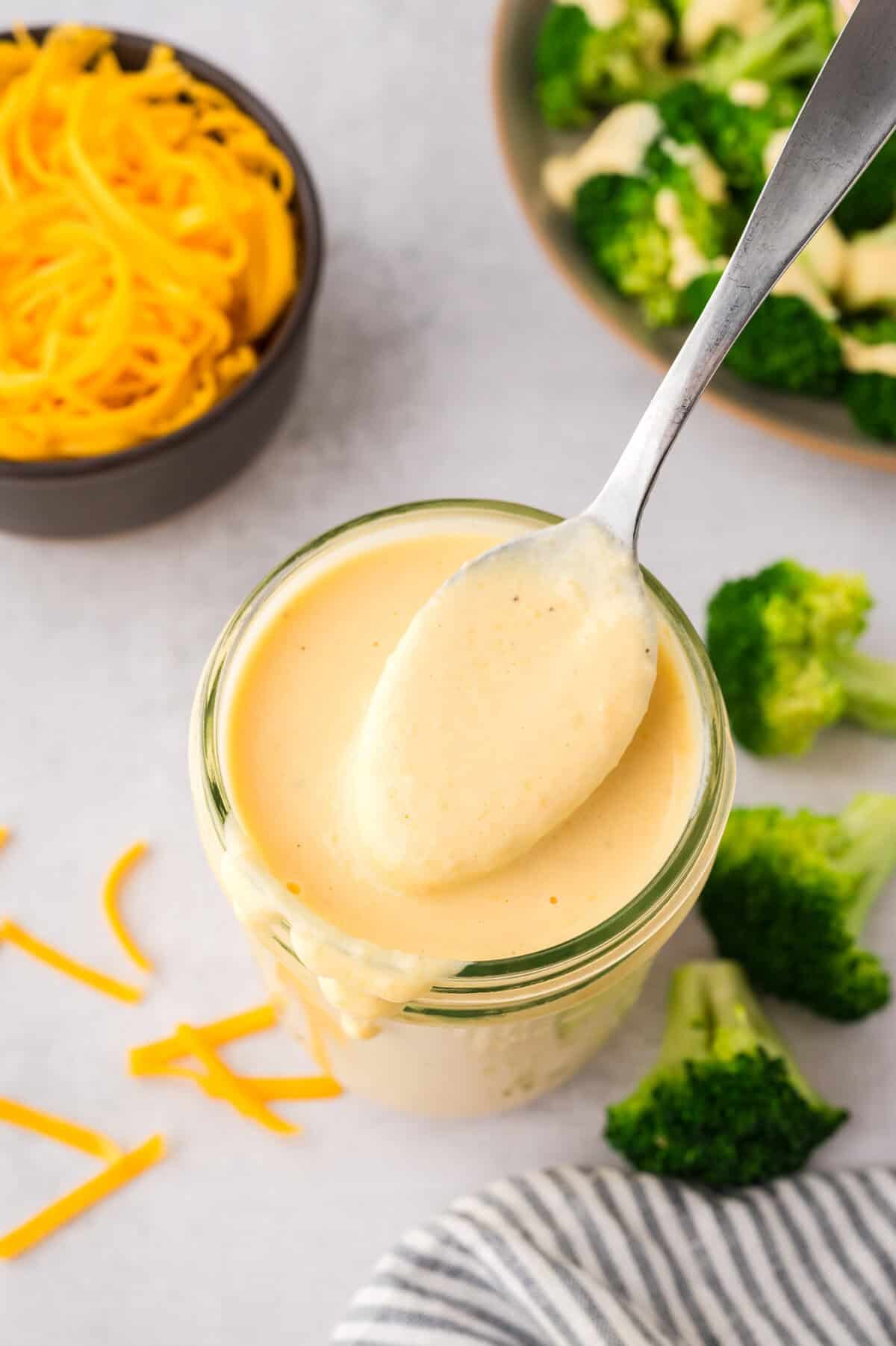 Spoon full of basic cheese sauce in mason jar.