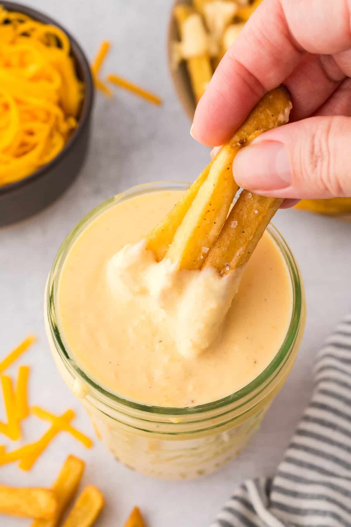 Fries being dipped in basic cheese sauce.