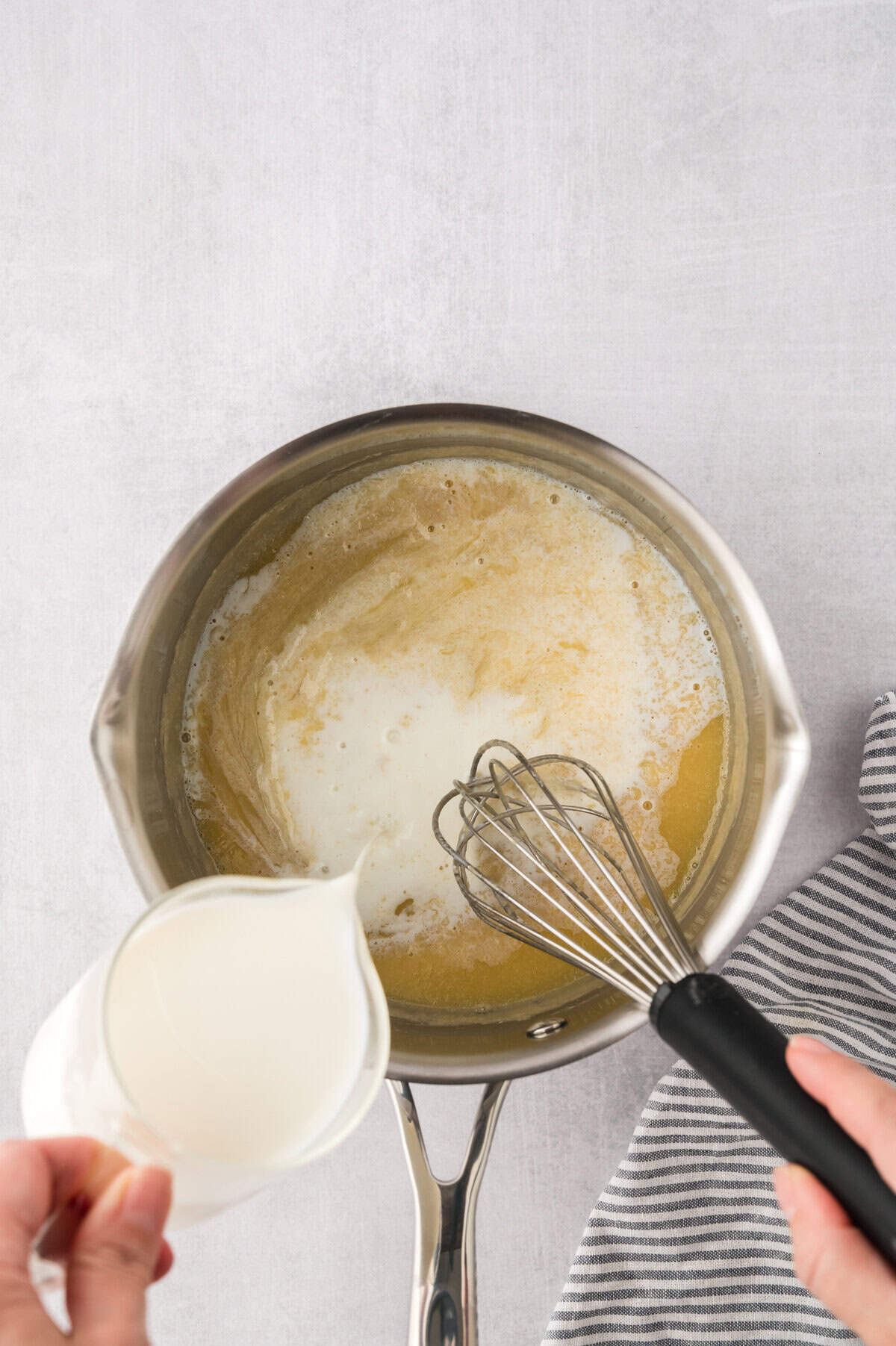 Milk being poured into a roux in a saucepan.