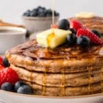 Stack of homemade pancakes being drizzled with maple syrup.