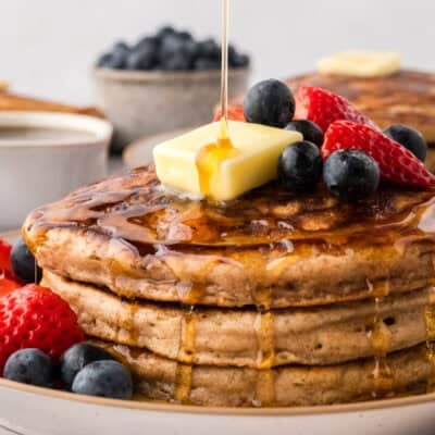 Stack of homemade pancakes being drizzled with maple syrup.