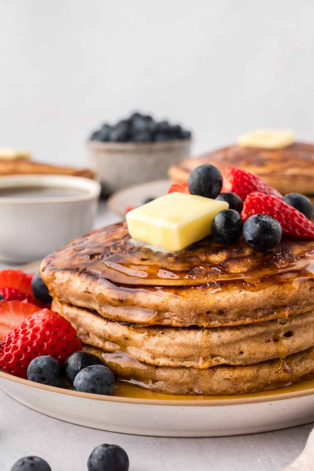 Stack of buttermilk pancakes topped with fresh berries, butter, and maple syrup.