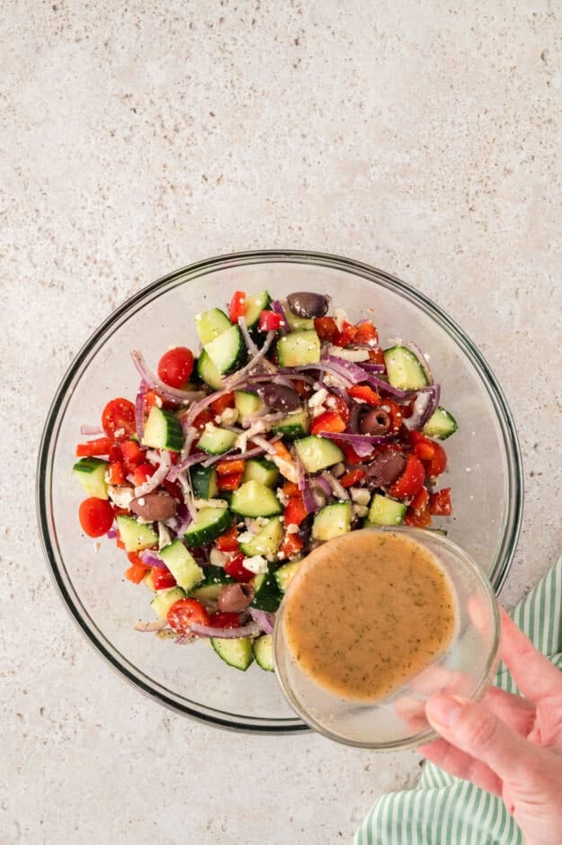 Greek dressing being poured over cucumber salad.