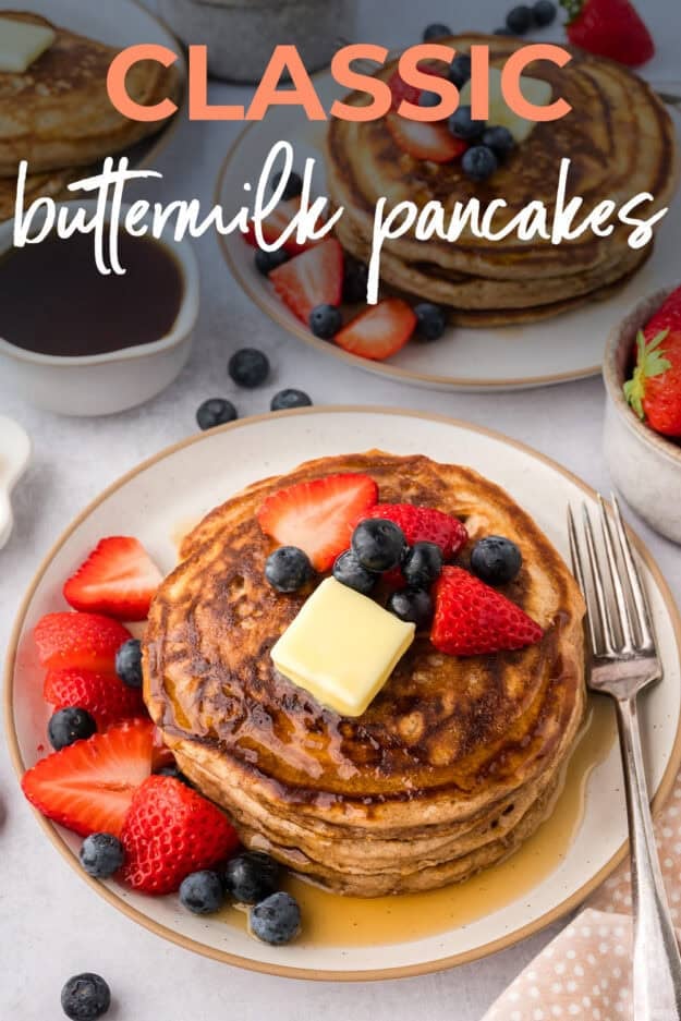 Homemade buttermilk pancakes on white plate topped with berries and butter.