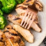 Sliced grilled chicken on plate with broccoli.
