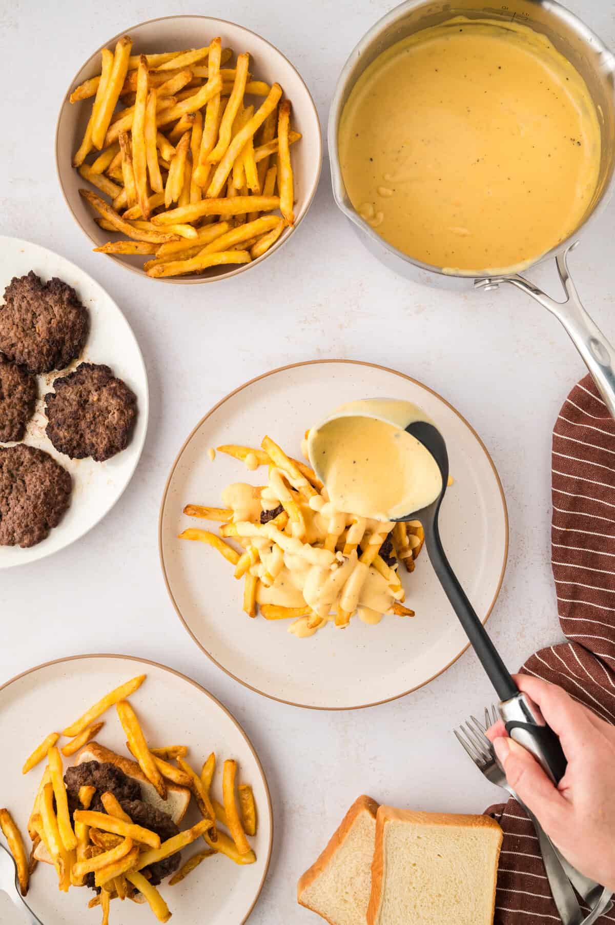 Beer cheese sauce being poured over burger and fries.