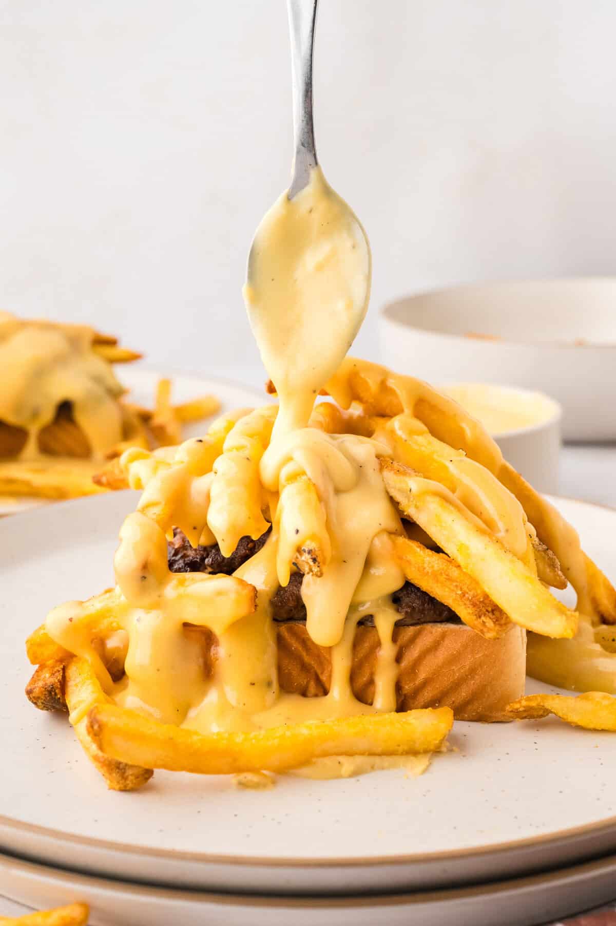Hamburger horseshoe sandwich being drizzled with cheese sauce.