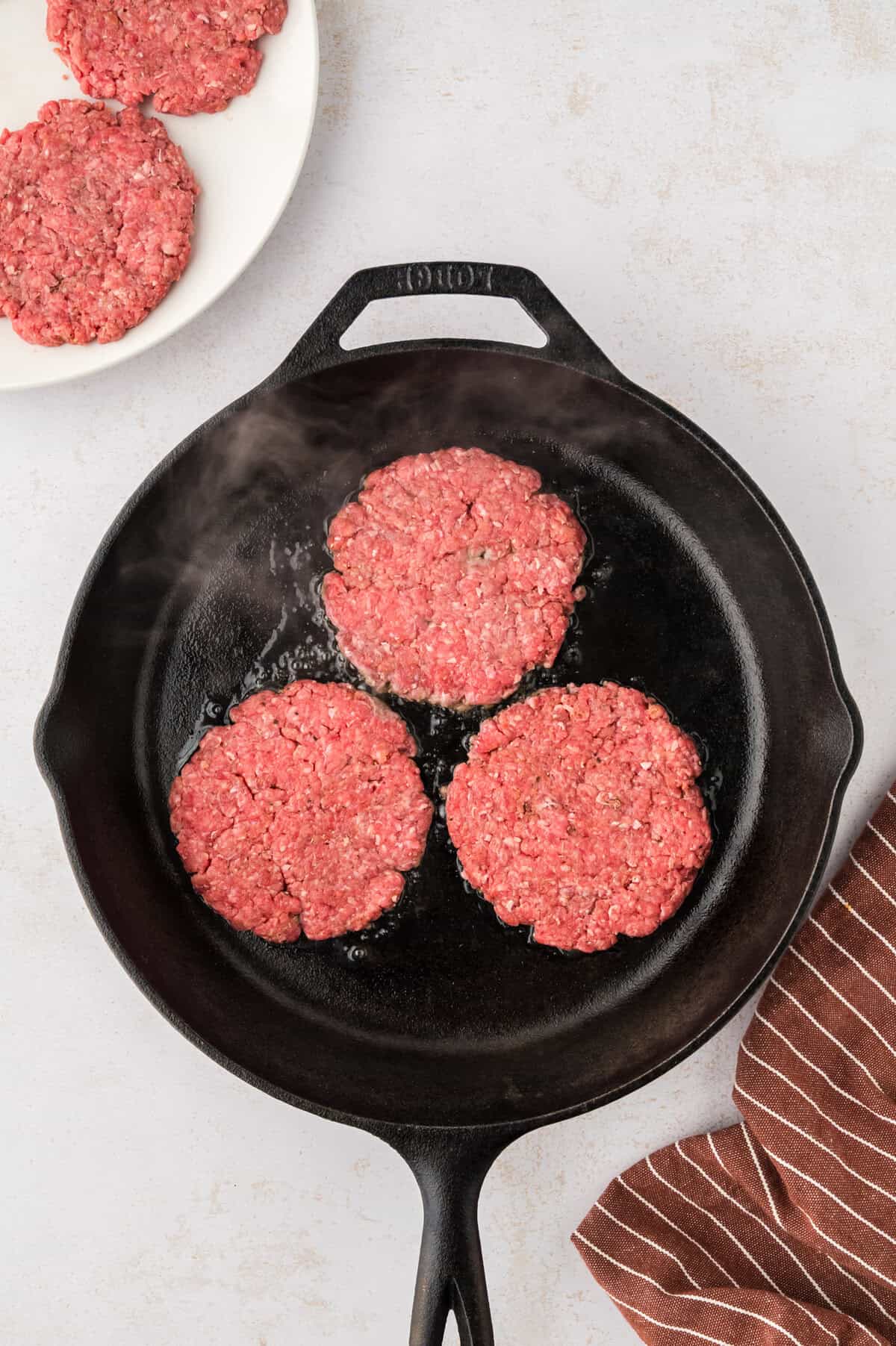 Hamburger patties being cooked in skillet.