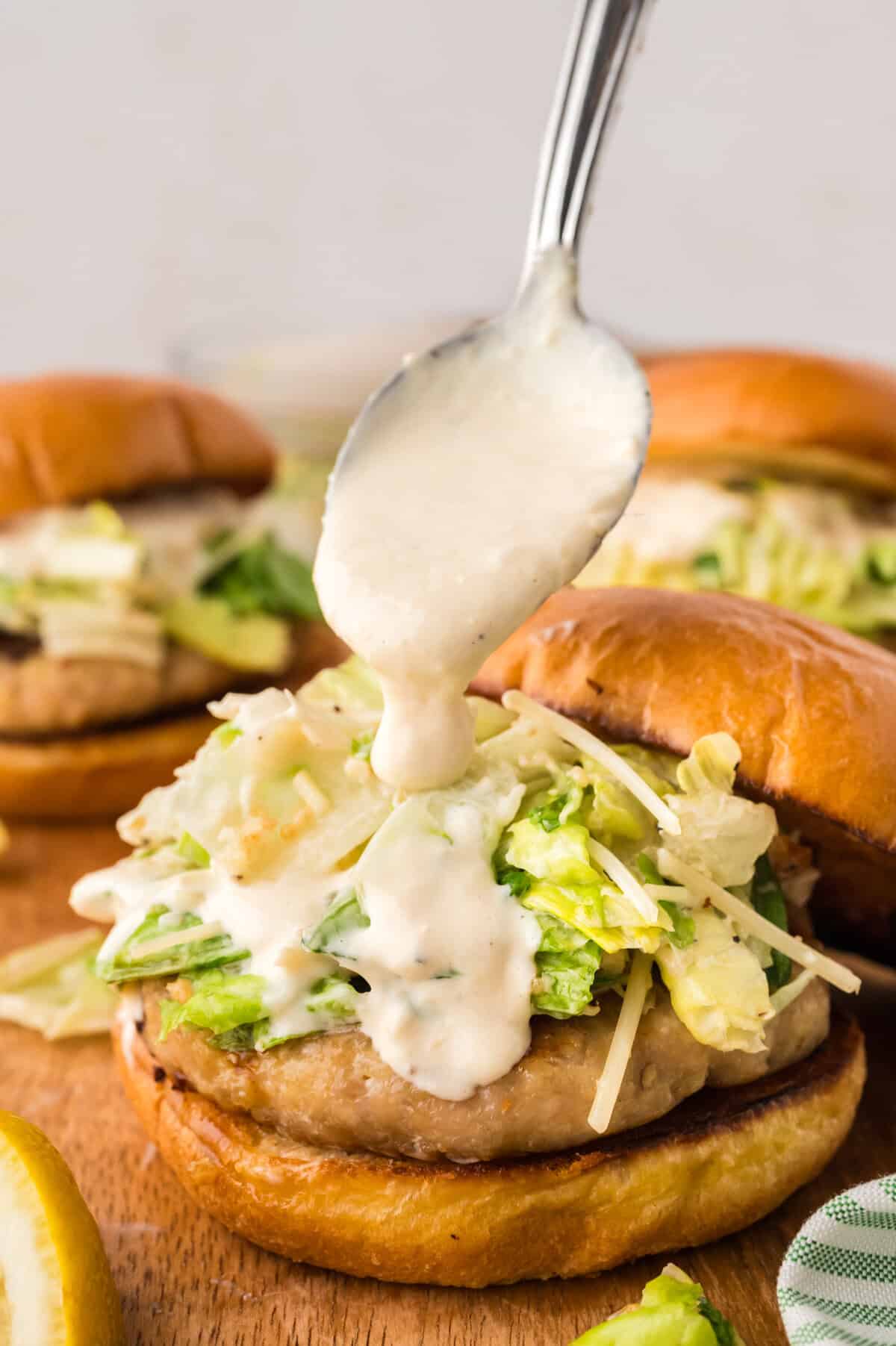 Caesar dressing being drizzled over salad topped burger.