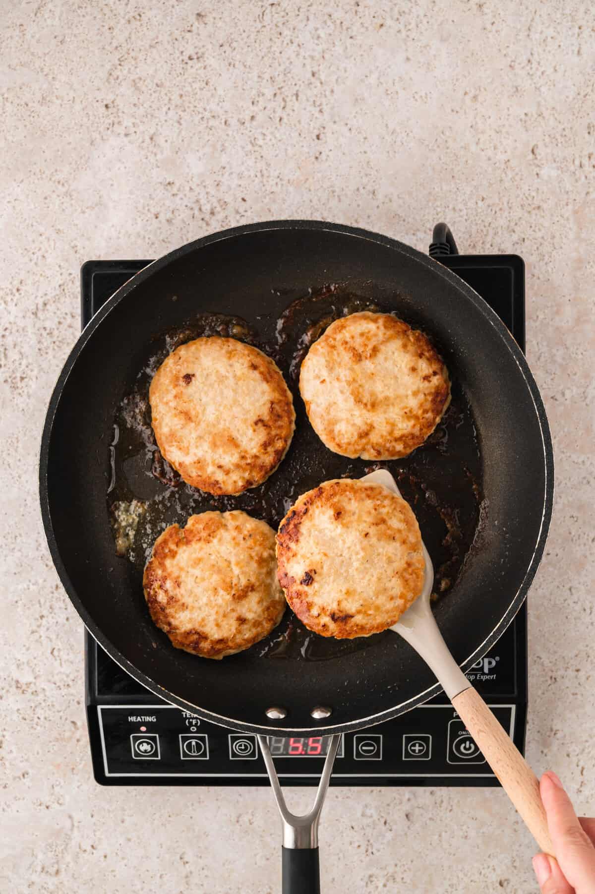 Chicken burgers cooking in skillet.