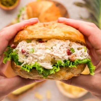 Hands holding a chicken salad sandwich made with bacon, pineapple, and jalapeno.