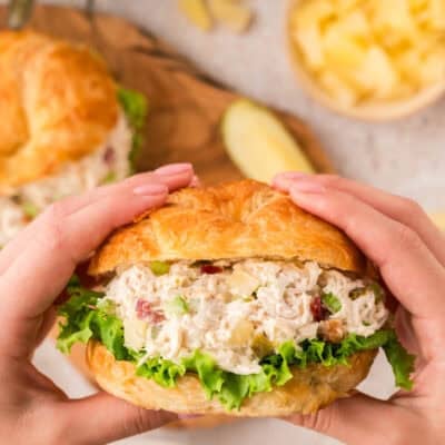 Hands holding a croissant filled with pineapple jalapeno chicken salad.