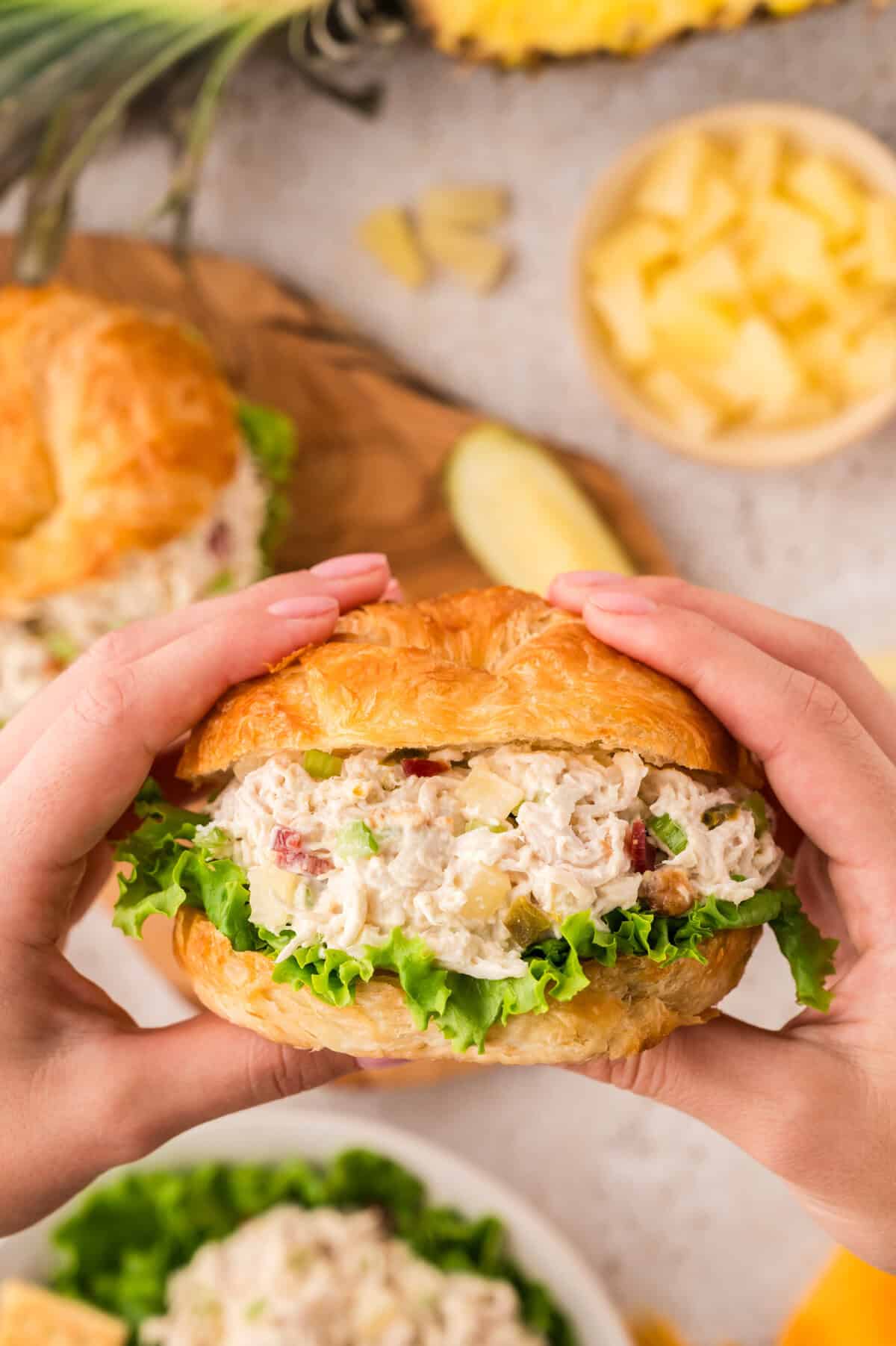 Hands holding a croissant filled with pineapple jalapeno chicken salad.