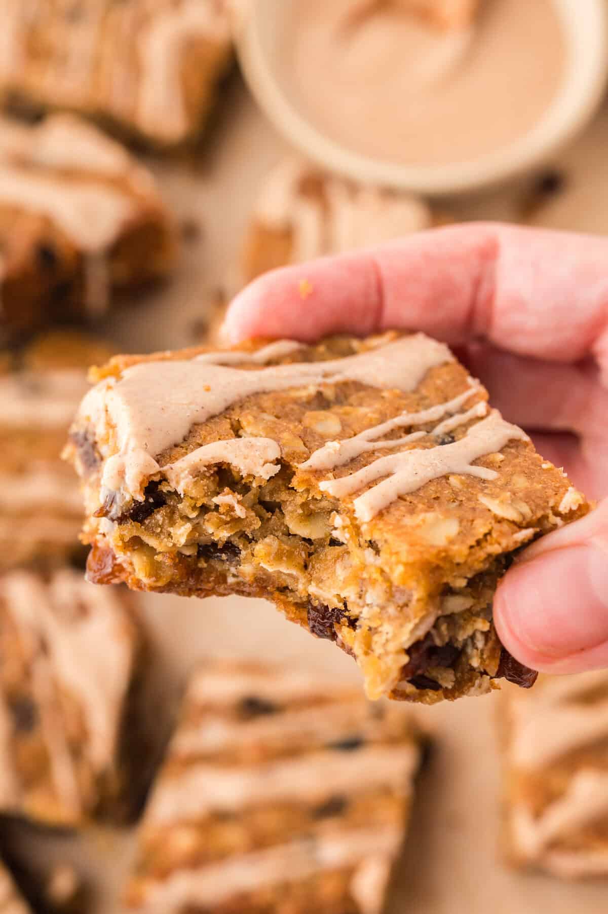 Hand holding an oatmeal raisin bar topped with glaze.
