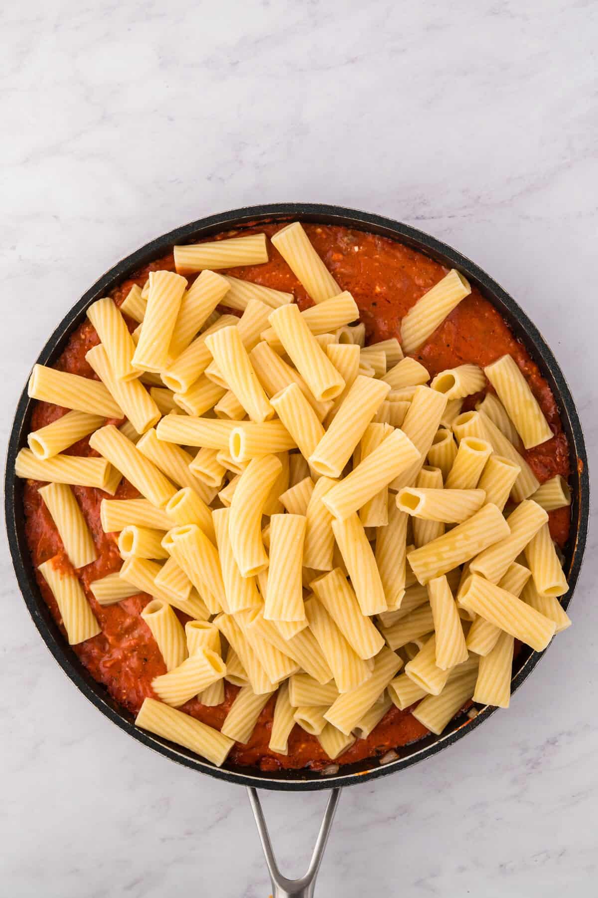 Rigatoni being stirred into pasta sauce.