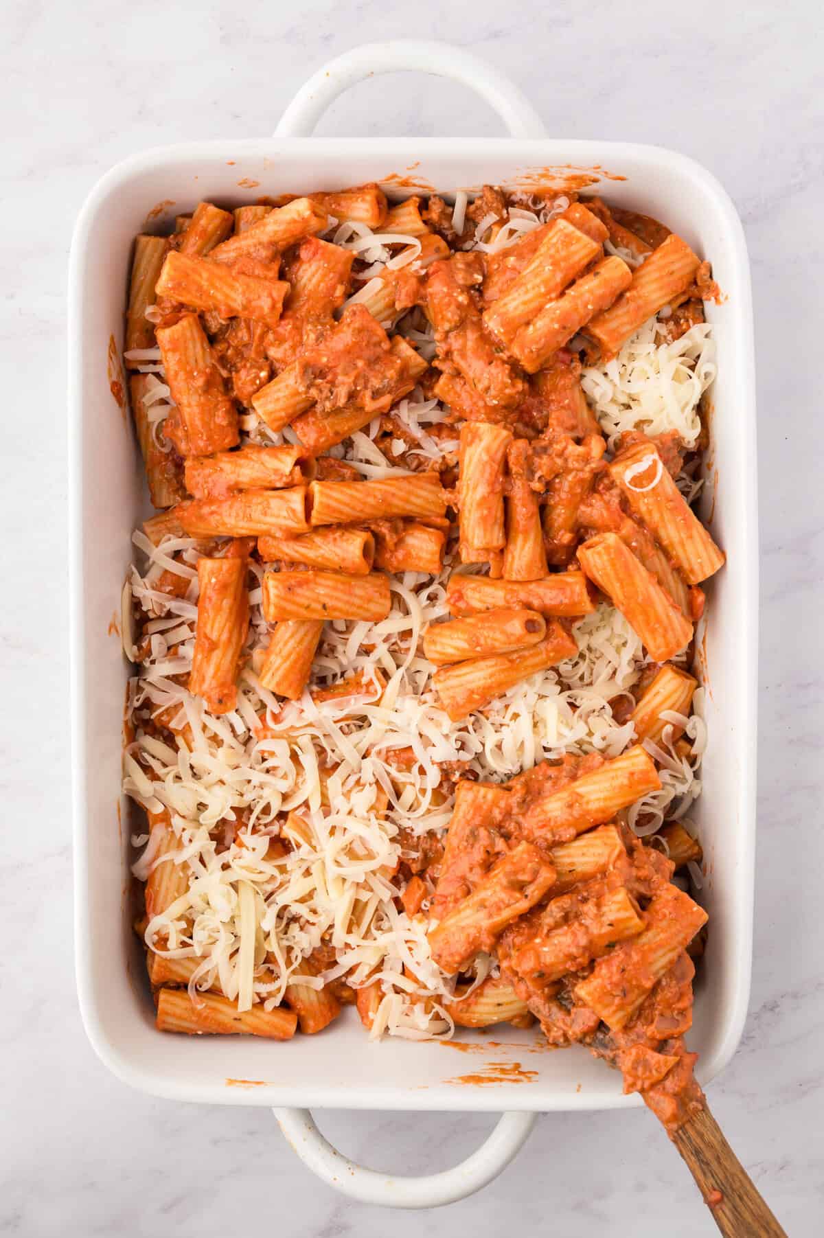 Rigatoni and cheese being layered in baking dish.
