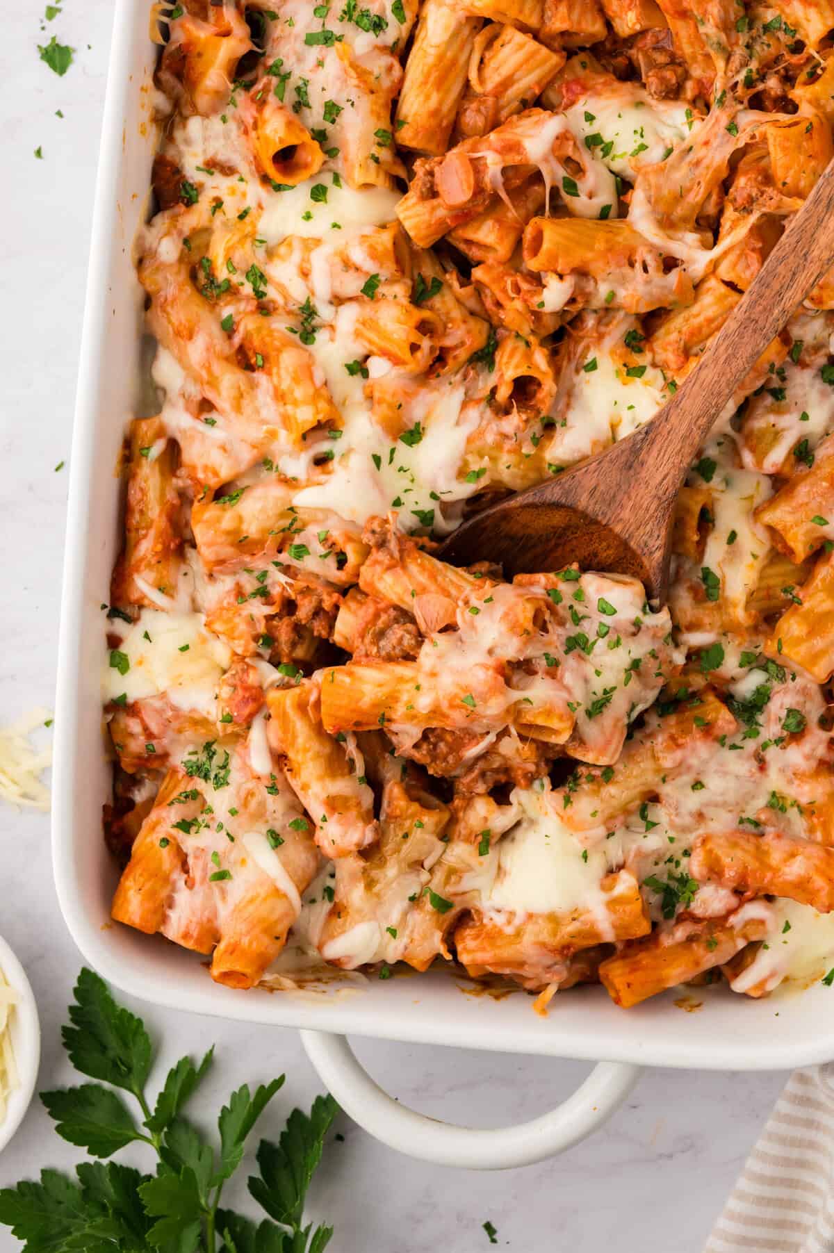 Wooden spoon in baking dish full of baked rigatoni.