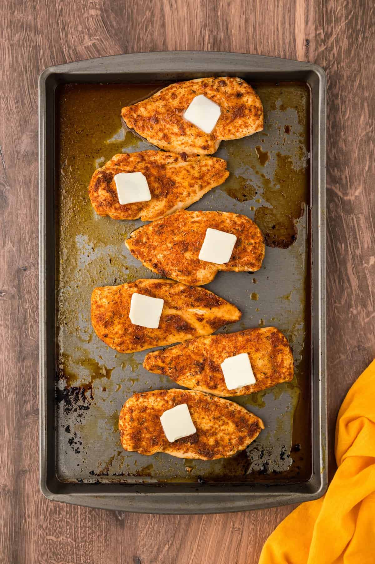 Baked chicken breasts topped with pats of butter.