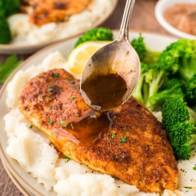 Pan sauce being drizzled over baked chicken breast.