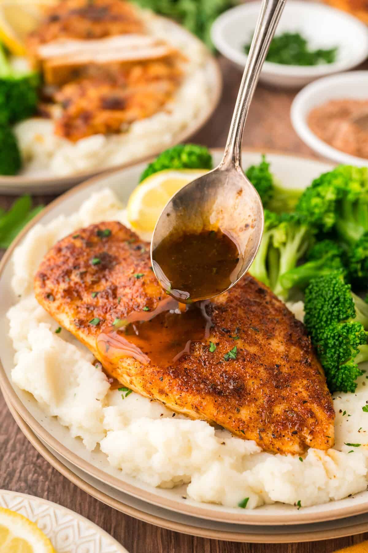 Pan sauce being drizzled over baked chicken breast.