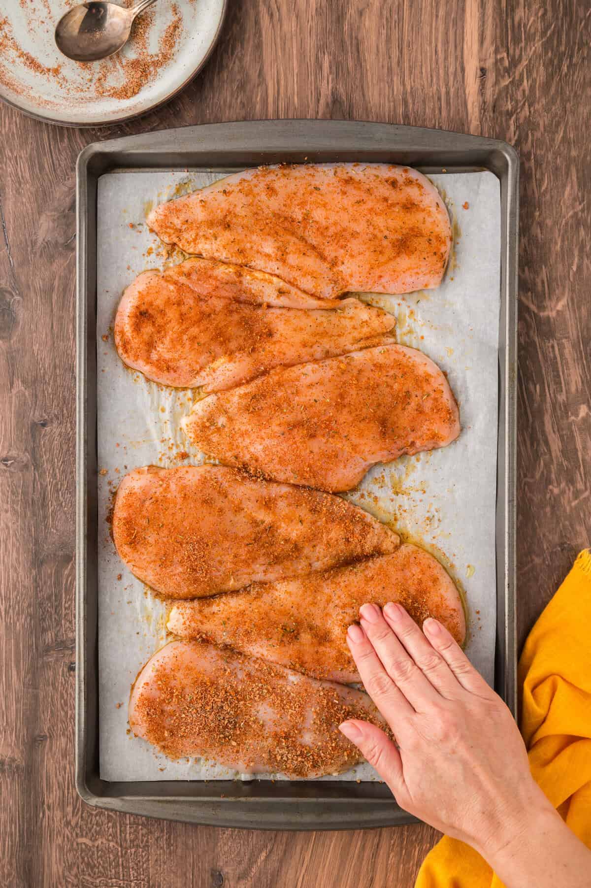 Hand rubbing seasoning over chicken breasts.