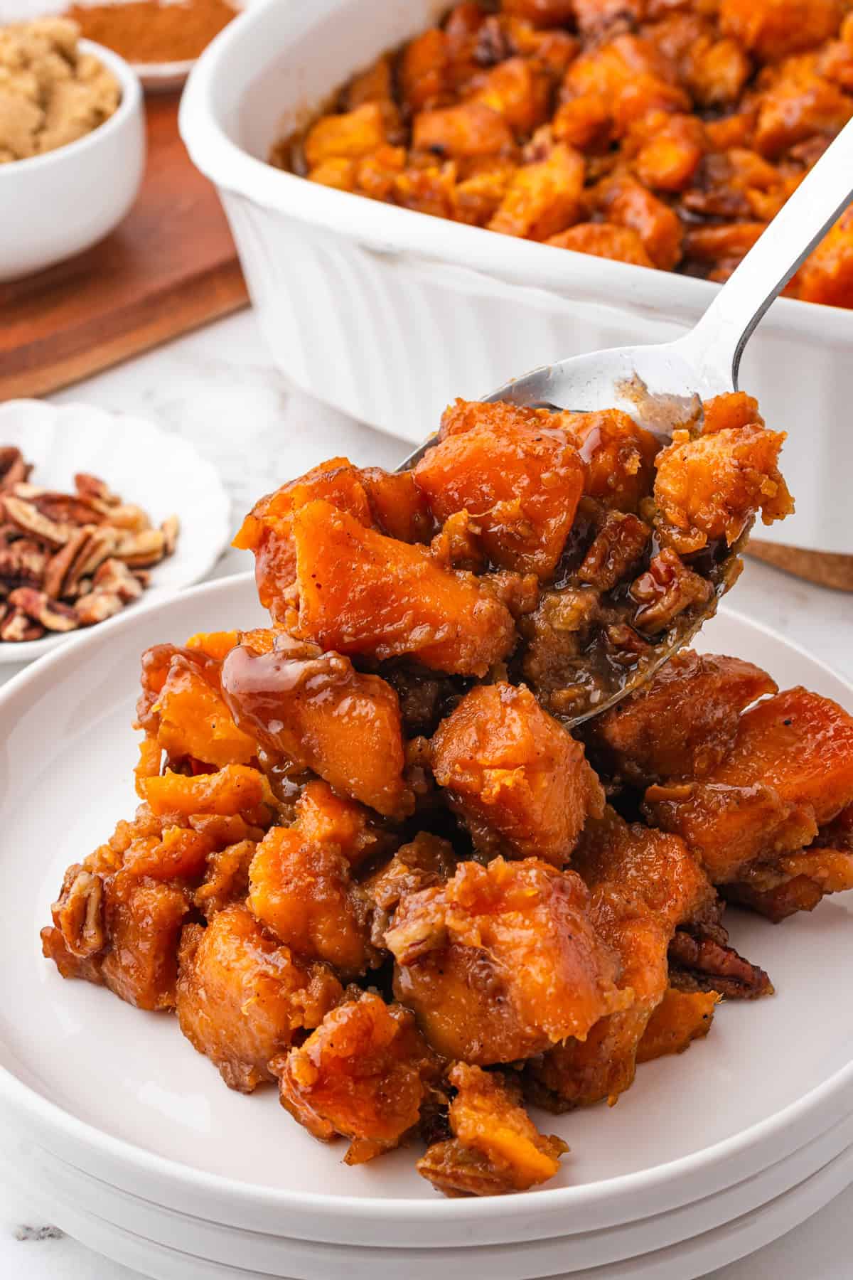 Candied yams being spooned on to white plate.