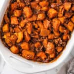 White casserole dish filled with candied yams topped with pecans.