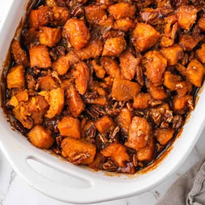 White casserole dish filled with candied yams topped with pecans.
