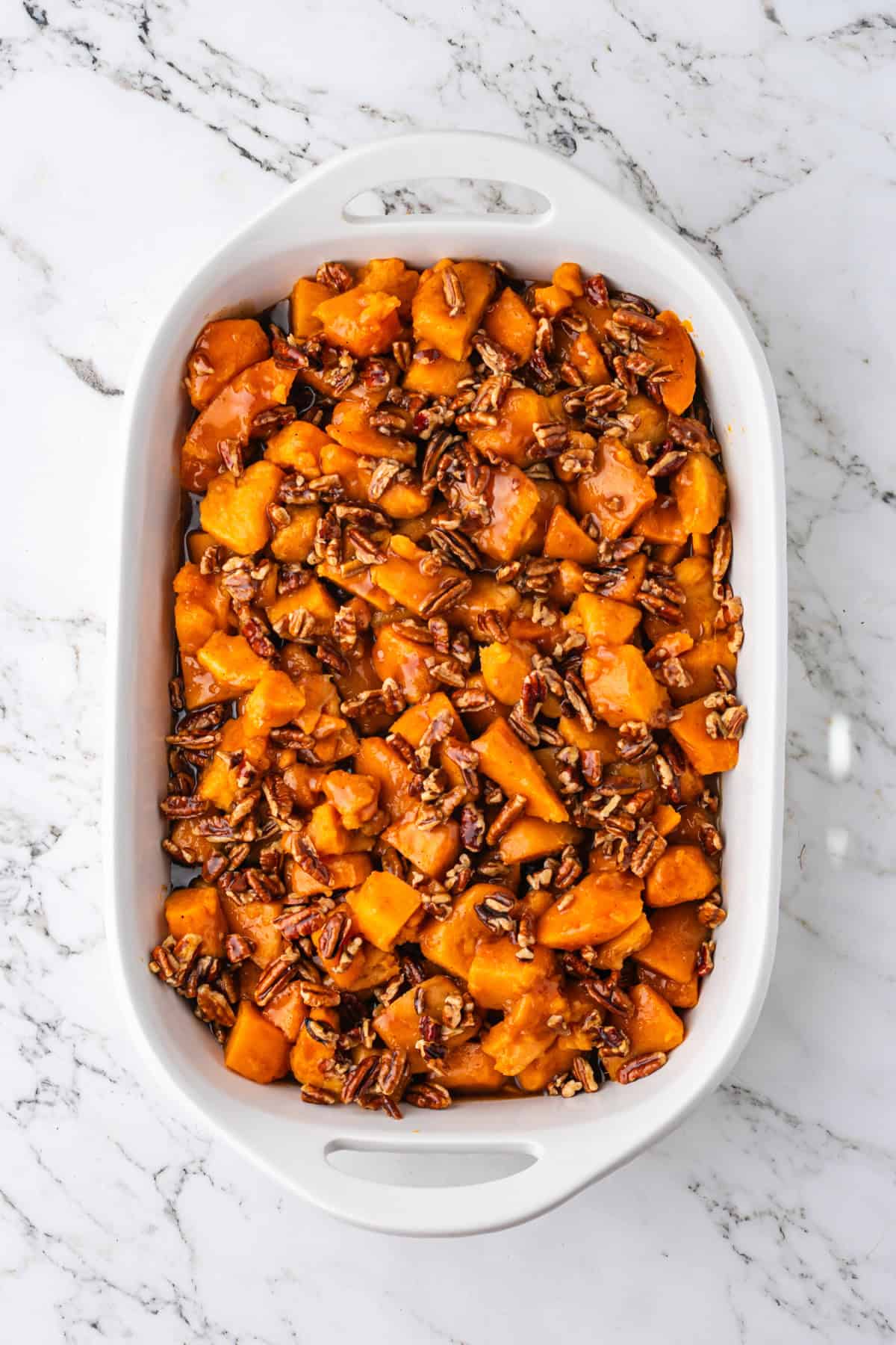 Candied yams topped with pecans and brown sugar glaze in baking dish.