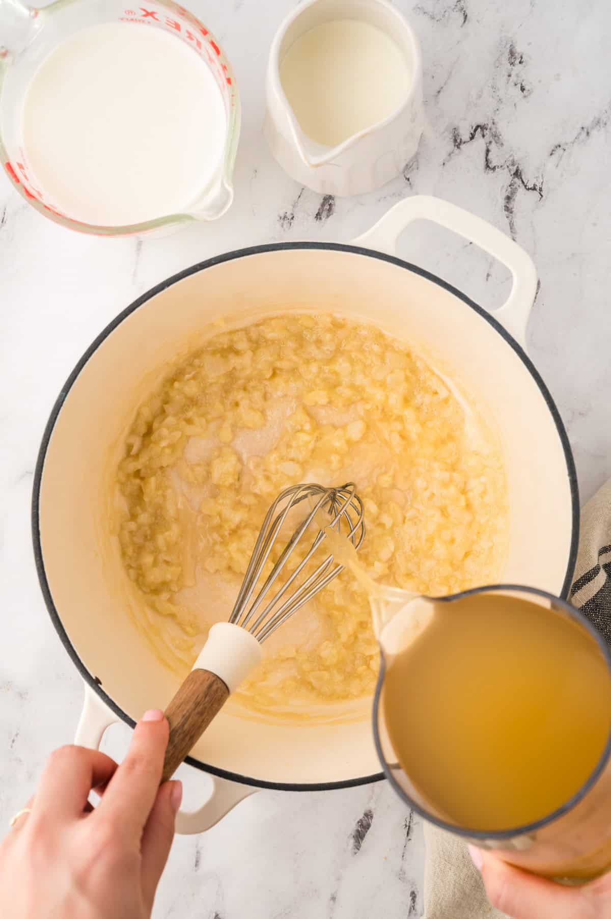 Chicken broth being poured over sauteed onions.