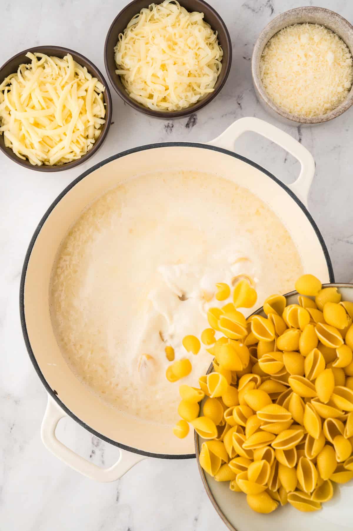 Dry pasta shells being added to soup.