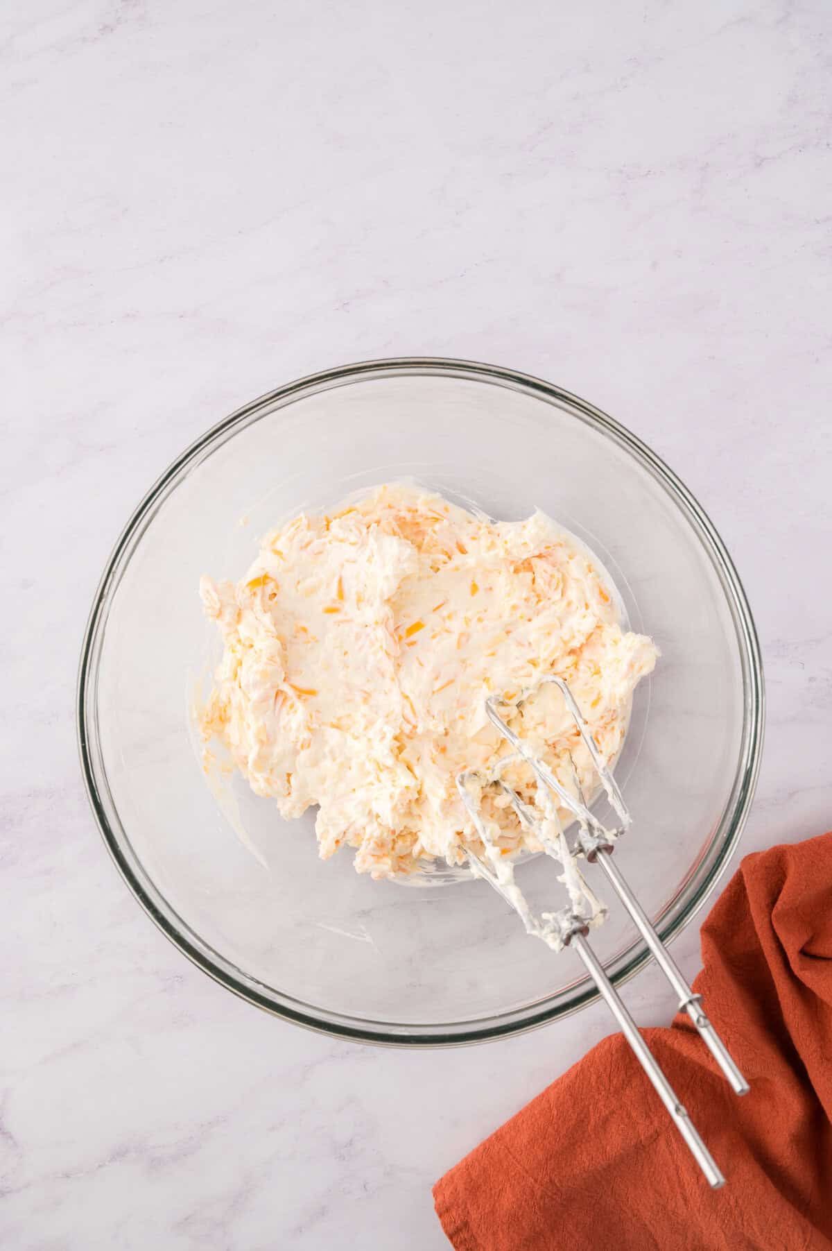 Cream cheese and shredded cheese beat together in a mixing bowl.