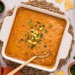 Baking dish filled with chicken enchilada dip and a spoon.